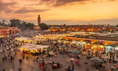 Marrakech’s vibrant Jemaa el-Fnaa square at sunset, bustling with stalls and visitors, with Koutoubia Mosque silhouetted against the skyline