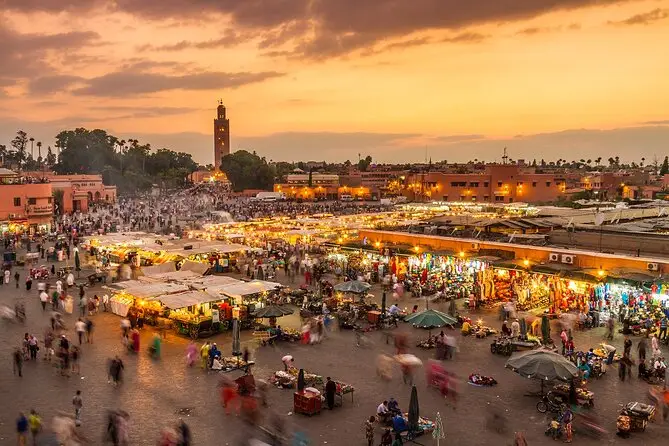Marrakech’s vibrant Jemaa el-Fnaa square at sunset, bustling with stalls and visitors, with Koutoubia Mosque silhouetted against the skyline