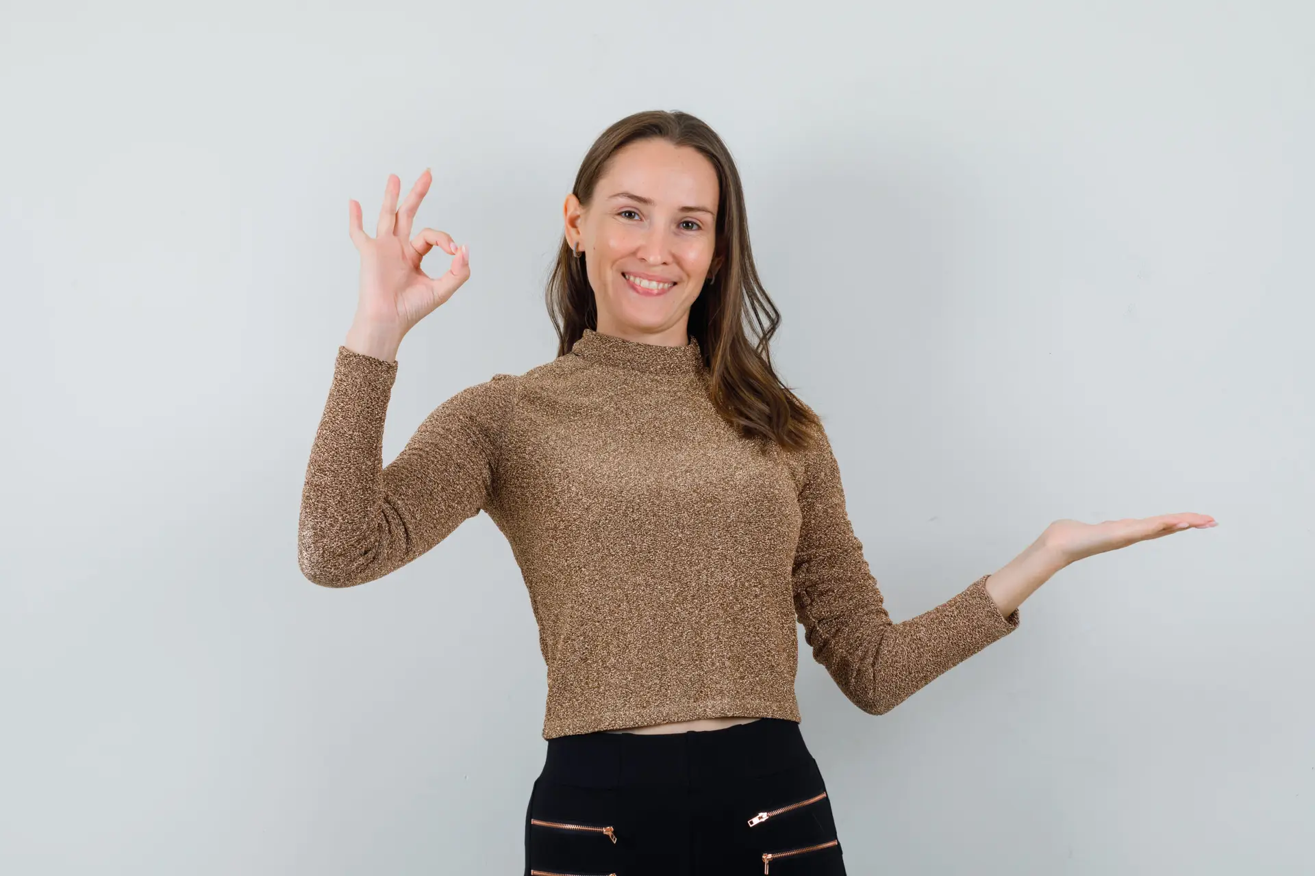 moroccan tours review young female showing ok gesture while raising hand up in golden blouse and looking glad. front view.